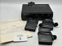 Photo of black Realistic FM wireless microphone receiver with power and three channel volume controls, and three matching wireless microphone transmitters laid out with attached lavalier headset microphones and cables, plus owner's manual.