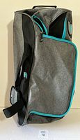 Side profile of gray rolling sport bag showing blue zipper accents, black handles and shape.
