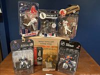 Six sports figures including baseball, football, and hockey in original packaging on display against blue background.