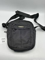 Front view of black Tracker crossbody bag showing main and front zippered compartments and adjustable strap with shoulder pad.