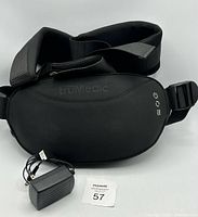 Black TruMedic heated massager laying flat with attached wide black strap and power adapter placed beside it.