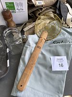Various kitchen and glassware items including boxed D'Ecco unbreakable champagne glasses, mason jar glasses, wooden pepper mill, aprons, tray, and skimmer.