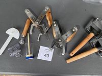 Top view of beekeeping tools including two metal frame grips with wooden handles, plastic bee escape tool, uncapping fork, and honey gate key