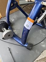 Photo showing blue metal frame of Cycl-O-Tron bike trainer with rubber foot pads and quick release skewer on surface nearby.
