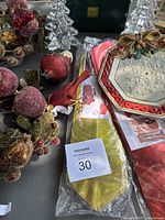 Christmas decorative items including sugared berry candle rings, red bird ornaments, small pine cone clusters, a red and white octagonal plate with embossed snowflake design and a gold decorative car bow in packaging.