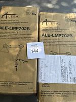 Photo showing two unopened boxes of Alera Architect Clamp-On Lamps model ALE-LMP702B with seller lot tag 144.