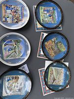 Six Limoges collectible plates depicting months with detailed colorful scenes and bordered edges, some square, some round, laid out on table with certificates visible.