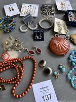 Full overhead photo of costume jewelry lot with earrings, necklaces, bracelets, and compact cases displayed on gray fabric.