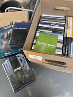 Photo of a box and pile containing roughly 30 DVD movies including a special edition Harry Potter box set and a 'Shrek the Third For Your Consideration 2007' DVD case on top.