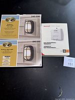 Two Hampton Bay exterior wall lights and one Honeywell thermostat in packaging.