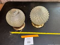 Two vintage glass globe ceiling bathroom lights with diamond textured pattern on glass globes, resting on brass-tone bases. Measuring tape shows approximately 8 inches in diameter.