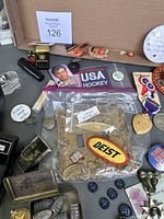 Overview of various vintage and military items including badges, pins, patches, coins, and bullets arranged in a box.