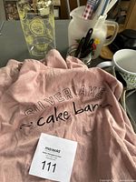 Pink Sir La Table apron with Silverlake cake bar text, ruffled bottom edge