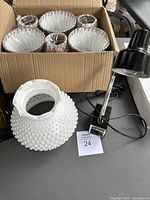 Box with 7 white hobnail lamp shades showing detailed texture, and front view of a black clamp style desk lamp with power cord