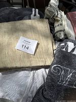 Beige embroidered blanket folded with West Elm throw pillow covers visible underneath in dark color.