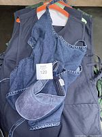 View of assorted cobbler aprons stacked including navy, green and denim with attached visor