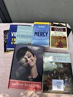 Lot of 8 hardcover books arranged in two rows with visible titles and covers showing variety including Audrey Hepburn biography and religious self-help books.