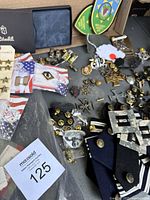 Photo showing assortment of military pins, buttons, rank insignias and patches along with a Zitchli wallet and Rothco canvas duffle bag.