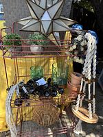 Full view of metal wire rack with shelves loaded with outdoor decorative items including pots, glass holders, macrame holders, and lights.
