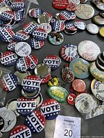 Top view showing numerous 'VOTE' buttons with red, white, and blue star designs, Robert Kennedy buttons, and various small pins scattered on a gray surface.
