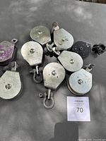 Overview of 11 assorted metal Campbell pulleys with various hooks and attachments on a gray surface.