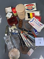 Overall view of various small collectibles arranged on a flat surface, including a carved stone donkey figurine missing part of its legs, multiple pens, a vintage pipe, a small clock, wooden box, decals, and a metal letter opener.