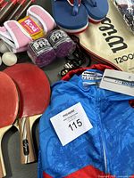 Lot contents showing cycling jersey, ping pong paddles and balls, tennis racket, boxing gloves, flip flops and Lakers basketball