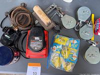 Overview of the lot on a grey table showing multiple tools and accessories including a hand plane, copper pipe clamps, pulleys, battery charger, and pack of screws.