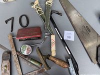 Various vintage tools laid out on table including saw blades, stapler, square, screwdriver, and gauge parts.