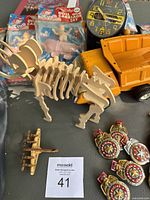 Wide shot of the vintage toys including the wooden dinosaur puzzle, wooden airplane, Tonka dump truck, badges, doll set, and clock in background