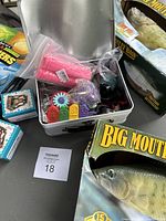 Overview of various items in a white box and adjacent boxes on table including pink bicycle grips, bass wall fish, and pencil sharpeners.
