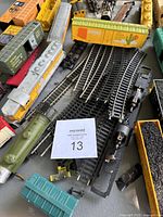 Photo of assembled and disassembled train cars with sections of black plastic train tracks on gray surface. Cars include colorful painted boxcars with state-themed designs.