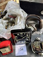 Photo showing two Westclox clocks (black wall clock and red travel alarm clock), headphones, and various small items including electronic parts packed in a plastic bag.