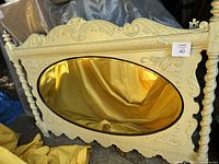 Front view of the yellow painted wooden vintage headboard with ornate carvings and oval inset mirror