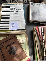 Top view of sheet music books stacked, showing titles including Seven Revolutionary Exercises and Rolling Stones Anthology.