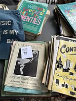 Photo showing vintage sheet music books and loose sheets including 'Great Music' with Artur Rubinstein and 'World's Greatest Hits of the Twenties.' Also visible is a blue tote bag with music-themed text.