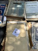Box of vintage sheet music showing multiple titles and folders with visible wear and aging.