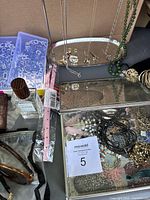 Photo showing West Elm glass jewelry box holding a variety of necklaces, bracelets, and jewelry items along with cologne, wallets, and sunglasses nearby