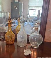 Three blown glass decanters displayed on wooden dresser surface reflecting in mirror. Includes amber crackled, clear round, and frosted etched horse decanters.