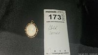 Cameo pin in setting next to MaxSold lot tag showing lot number