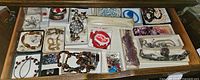 Top view of the drawer showing a variety of costume jewelry including bracelets, necklaces, shoe clips, and loose stones arranged in small compartments and bags.