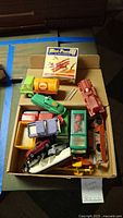Box containing various diecast and plastic trucks including Shell tanker, fire truck, and a small helicopter.