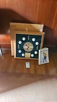 Wall clock featuring golf balls arranged around the clock face, small golf flags, and an engraved plaque below the clock. The clock measures about 17.5x17.5 inches. Includes the original box behind the clock.