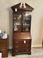 Full frontal view of the Jasper cherry wood Chippendale style secretary desk showing the two glass doors of the upper bookcase, the pediment top with finial, drop-front desk, and three bottom drawers with brass hardware.