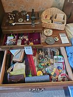 Full view of wooden jewelry box with cuff links, coins, vintage Sucrets tins, wicker basket with pins and bobby pins, assorted personal care items and small purses in dresser drawer.