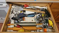 Drawer full of assorted kitchen utensils and gadgets including rolling pins, graters, can openers, scoops, and tongs