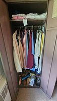 Closet with assorted ladies' clothing in various colors including sweaters, sweatshirts, shirts, jackets and trousers, with some items folded on top shelf and shoe stretchers on floor