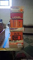Stack of seven Lionel train accessory boxes showing No. 110 and No. 111 Trestle Sets, 3 Operating Street Lamps, and other boxed Lionel items in a basement setting