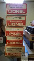 Stack of 5 Lionel train car boxes showing model names and numbers: Illuminated Pennsylvania Baggage Car, Times Square Passenger Car, Pennsylvania Square Passenger Car, Washington Circle Passenger Car, Pennsylvania Diesel Switcher.