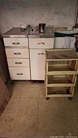 Wide view of two vintage metal cabinets and plastic storage bin cart on wheels in a basement setting.